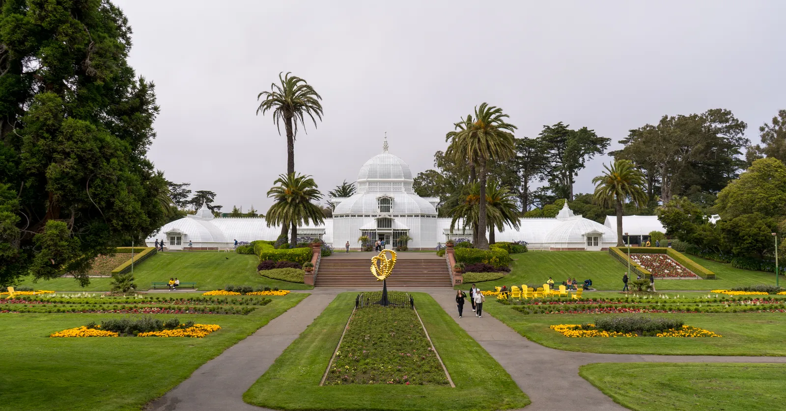 The Conservatory of Flowers in Golden Gate Park, a white Victorian glasshouse with a domed centre standing above formal flowerbeds and lawns with palms on either side