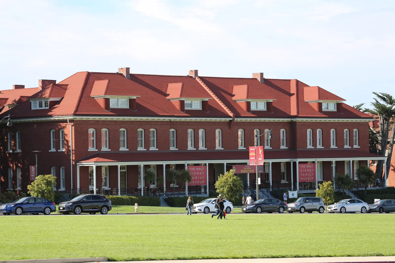 The Walt Disney Family Museum in San Francisco, a long red-brick barracks with a red tiled roof and dormer windows, seen across the grass of the Presidio's main parade ground