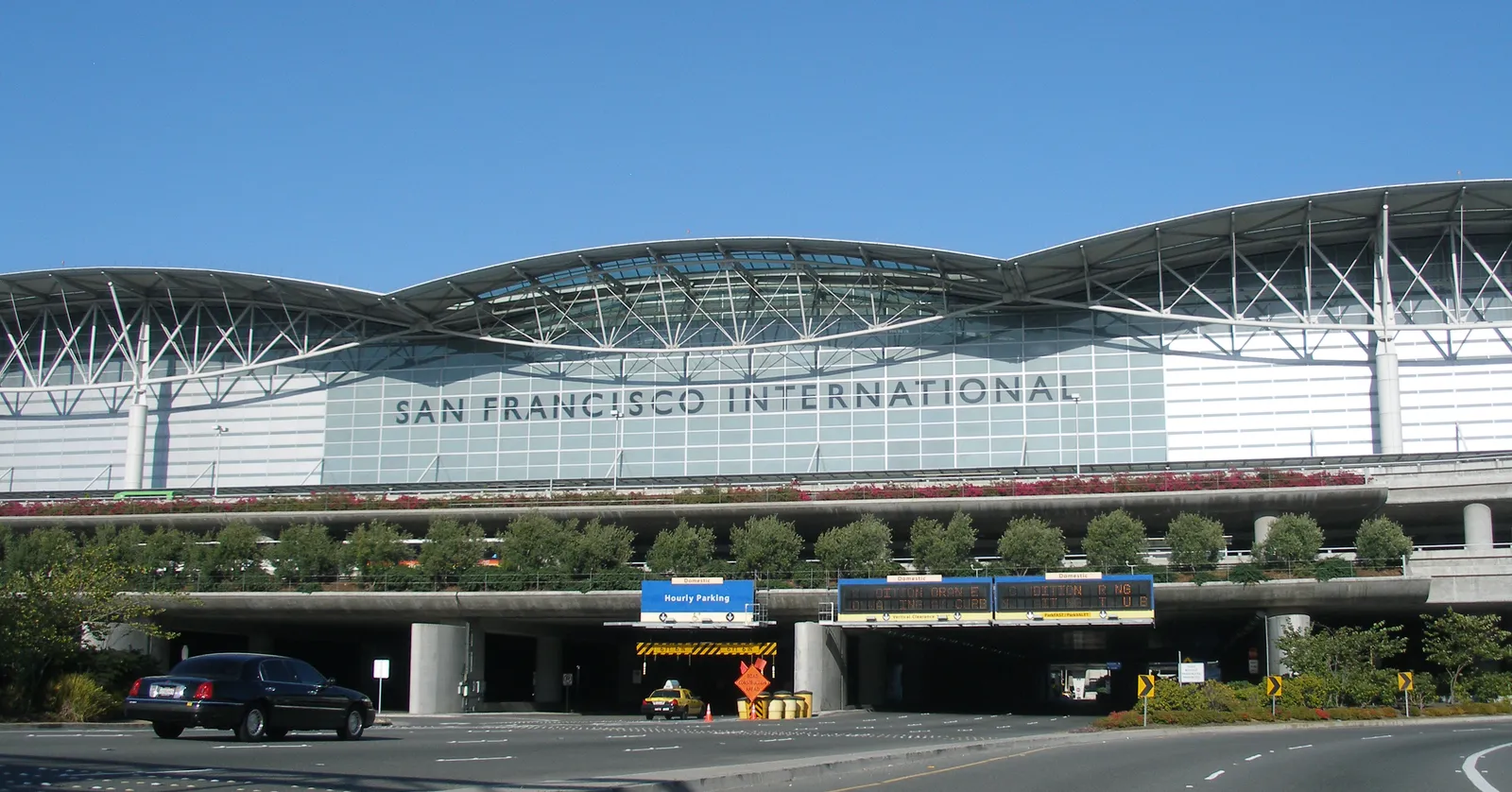 The front of the International Terminal at San Francisco International Airport, a long glass facade under a curved white roof with SAN FRANCISCO INTERNATIONAL lettered across it and the departures roadway below