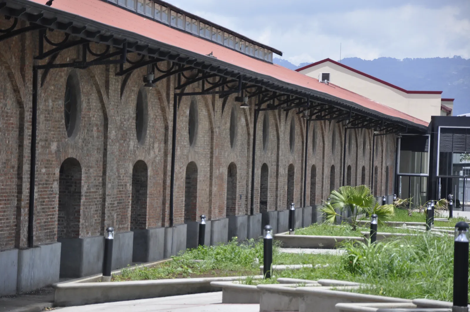The long brick flank of the old customs warehouse in San Jose, a row of arched windows under an iron-bracketed canopy and a red roof, with mountains behind