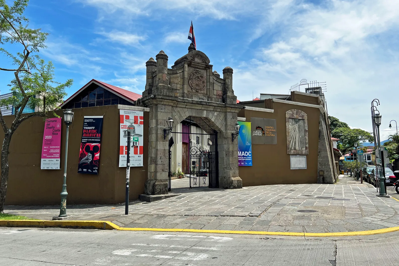 The carved stone gateway of the old national liquor works in San Jose, iron gates between two pinnacles, with exhibition banners hung on the ochre walls either side