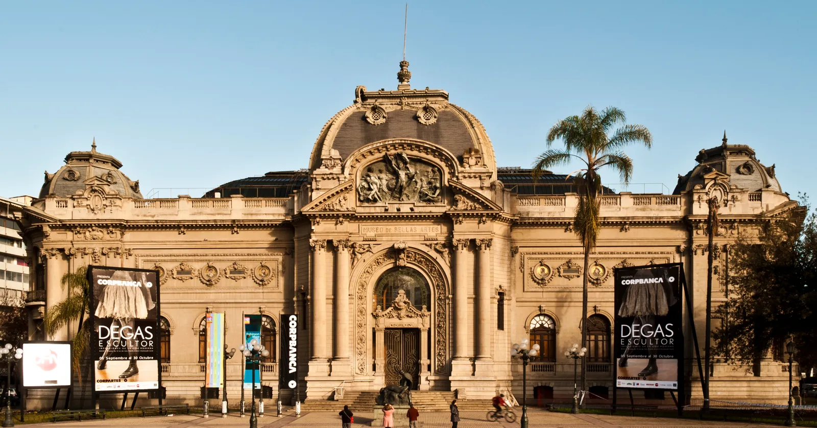 The ornate stone facade of Chile's National Museum of Fine Arts in Santiago, with a domed glass roof behind its central arched entrance and palms at either side