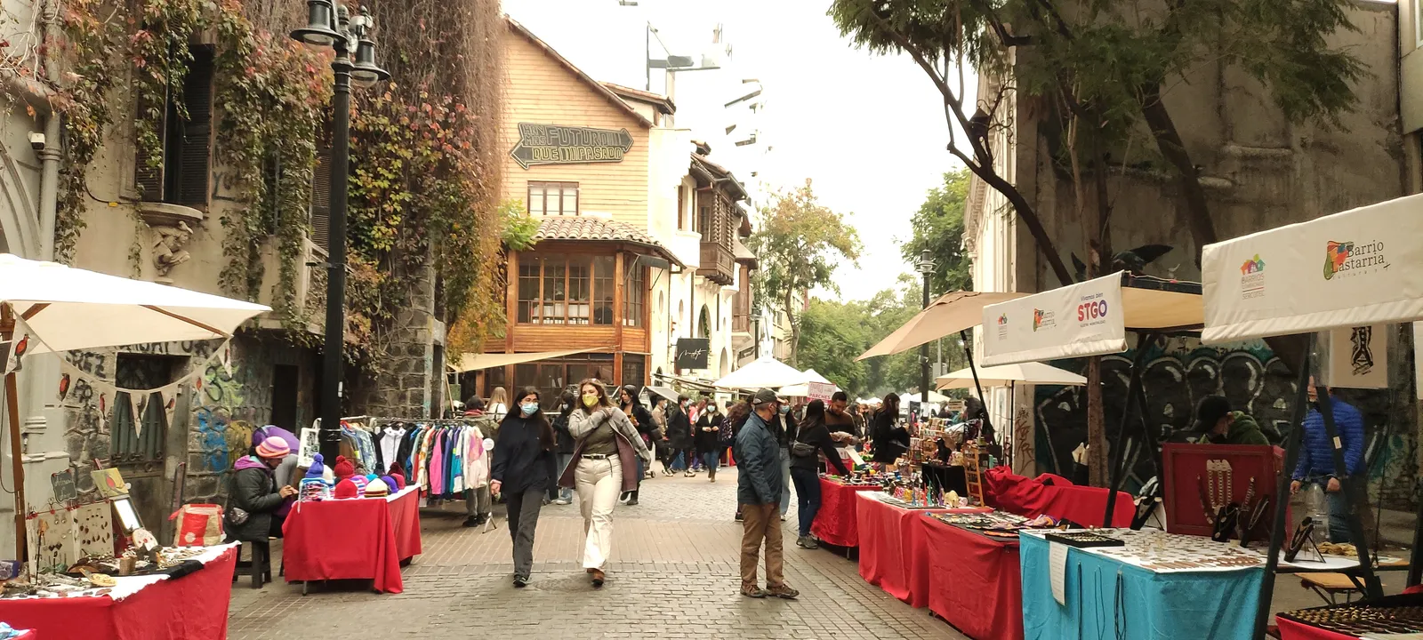 Craft stalls with red cloths set out along a cobbled street in Barrio Lastarria, Santiago, beneath ivy-covered stone buildings and a tiled roofline