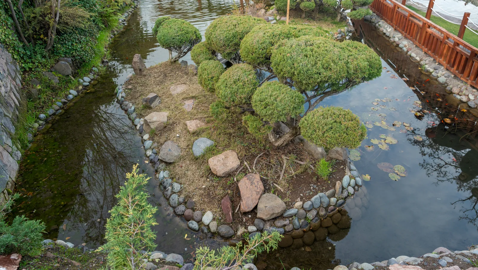 A clipped island of shrubs and boulders in the still pond of the Japanese Garden on Cerro San Cristóbal, Santiago, edged with river stones and timber railings