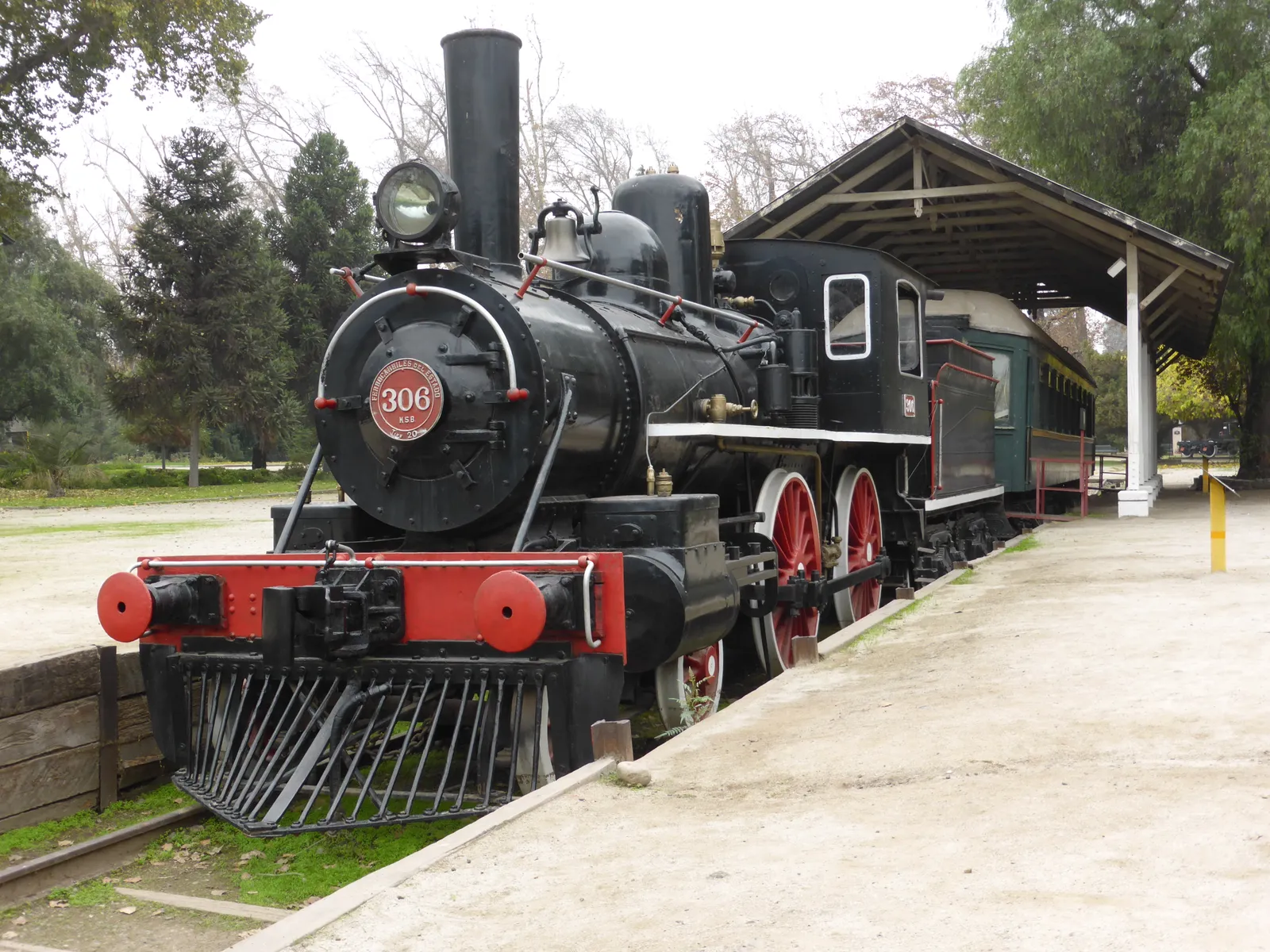 A black steam locomotive numbered 306 with red wheels and a cowcatcher, standing on preserved track under an open shelter at Santiago's railway museum