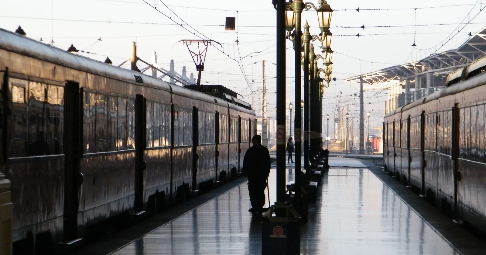 Two long trains standing either side of a wet platform at Estación Central in Santiago, under ornate lamp standards and the iron roof of the train shed