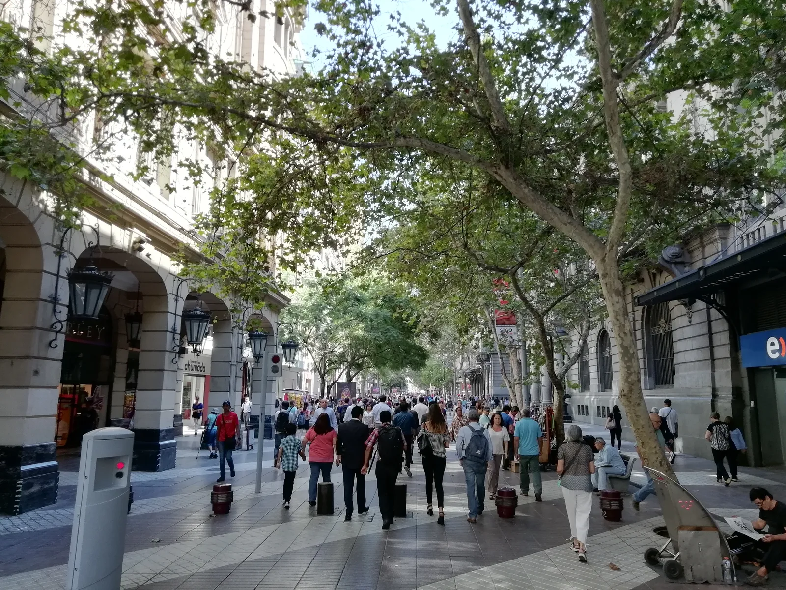 Crowds walking down the tree-shaded pedestrian street of Paseo Ahumada in central Santiago between tall stone-fronted buildings