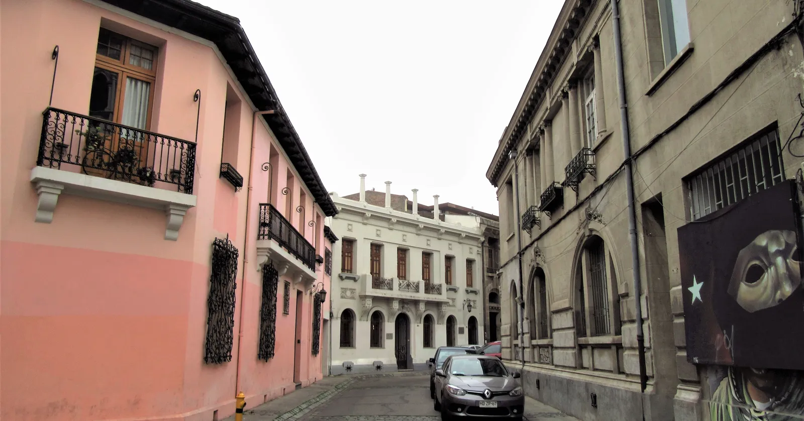 A narrow curved street in Barrio Concha y Toro, Santiago, with a pink corner mansion and wrought-iron balconies on the left and pale neoclassical facades closing the view ahead