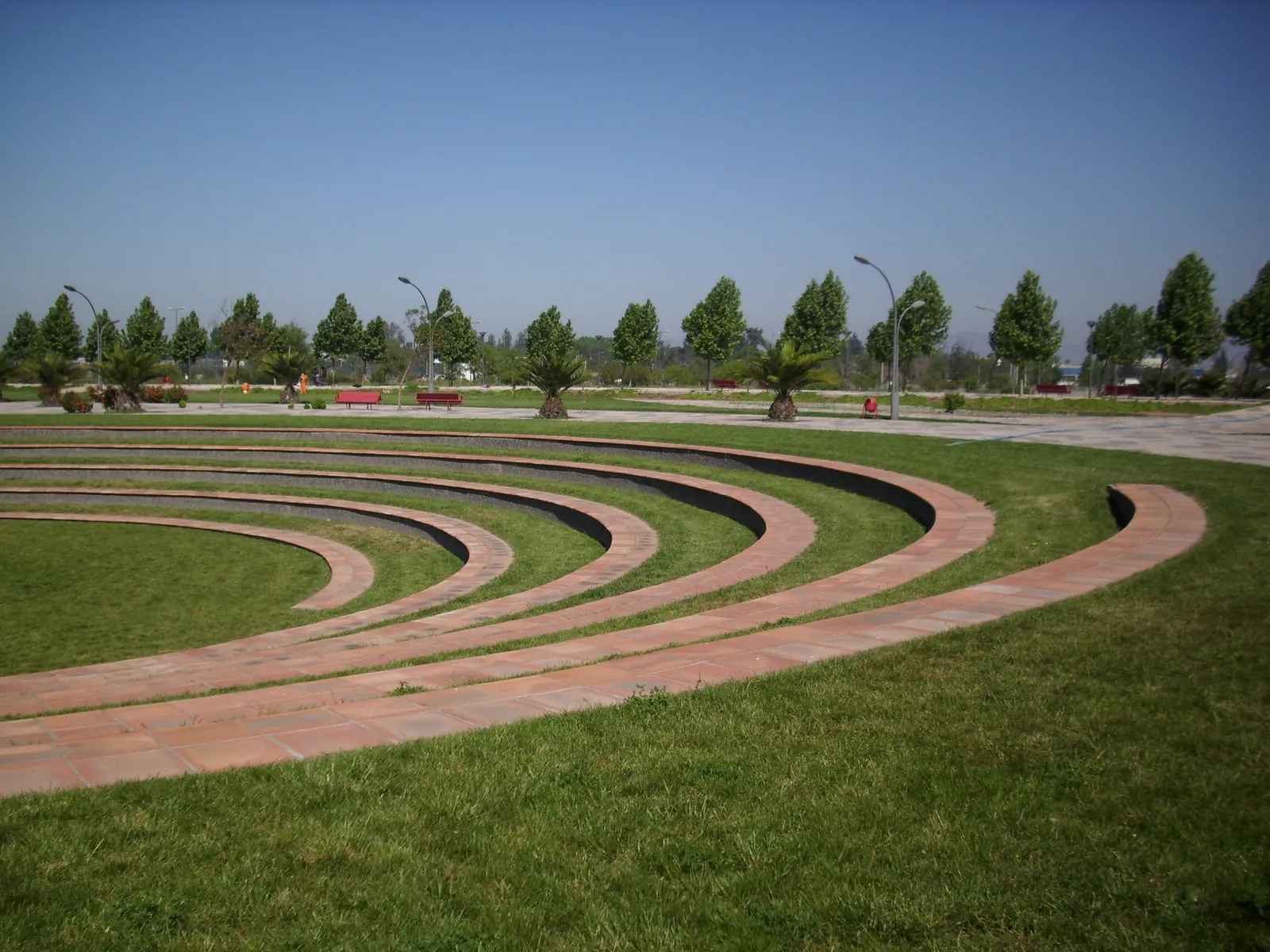 Curved brick and grass terraces of an open-air amphitheatre in Parque Bicentenario at Cerrillos, Santiago, with young trees and flat lawns behind it