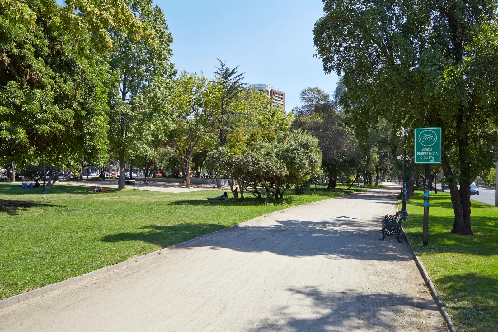 A wide gravel path through Parque Balmaceda in Providencia, Santiago, with lawns and mature trees either side and an apartment block visible beyond