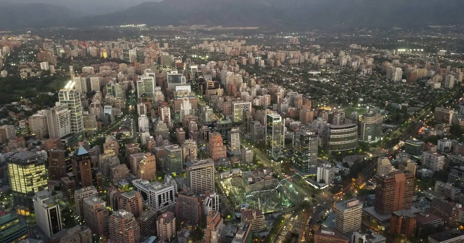 Providencia seen from the Sky Costanera observation deck at dusk, a grid of lit towers and streets running out to the dark wall of the Andes