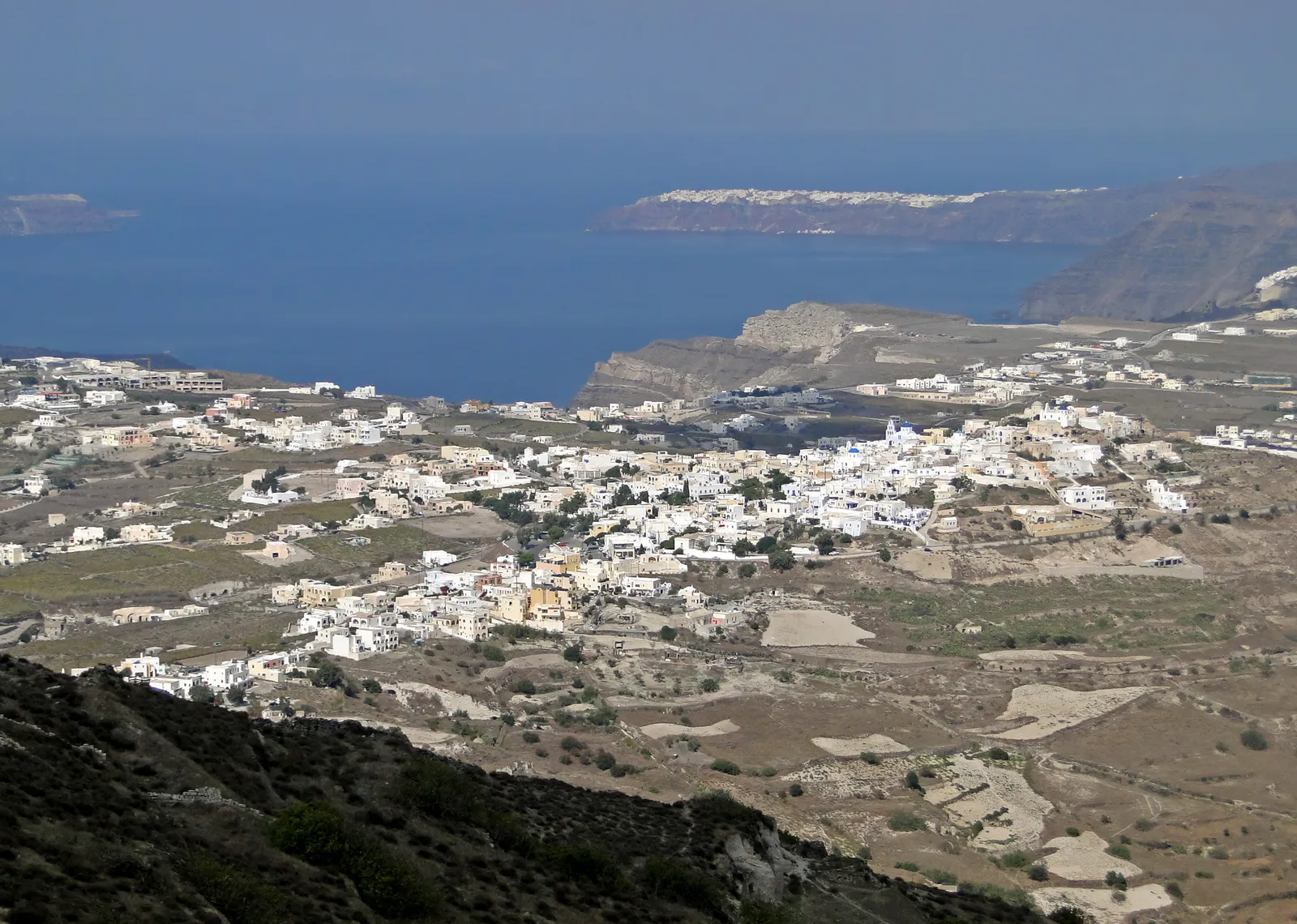 Pyrgos spread over its hill in low white and ochre houses, with cultivated terraces below it and the caldera and the far crater rim visible beyond