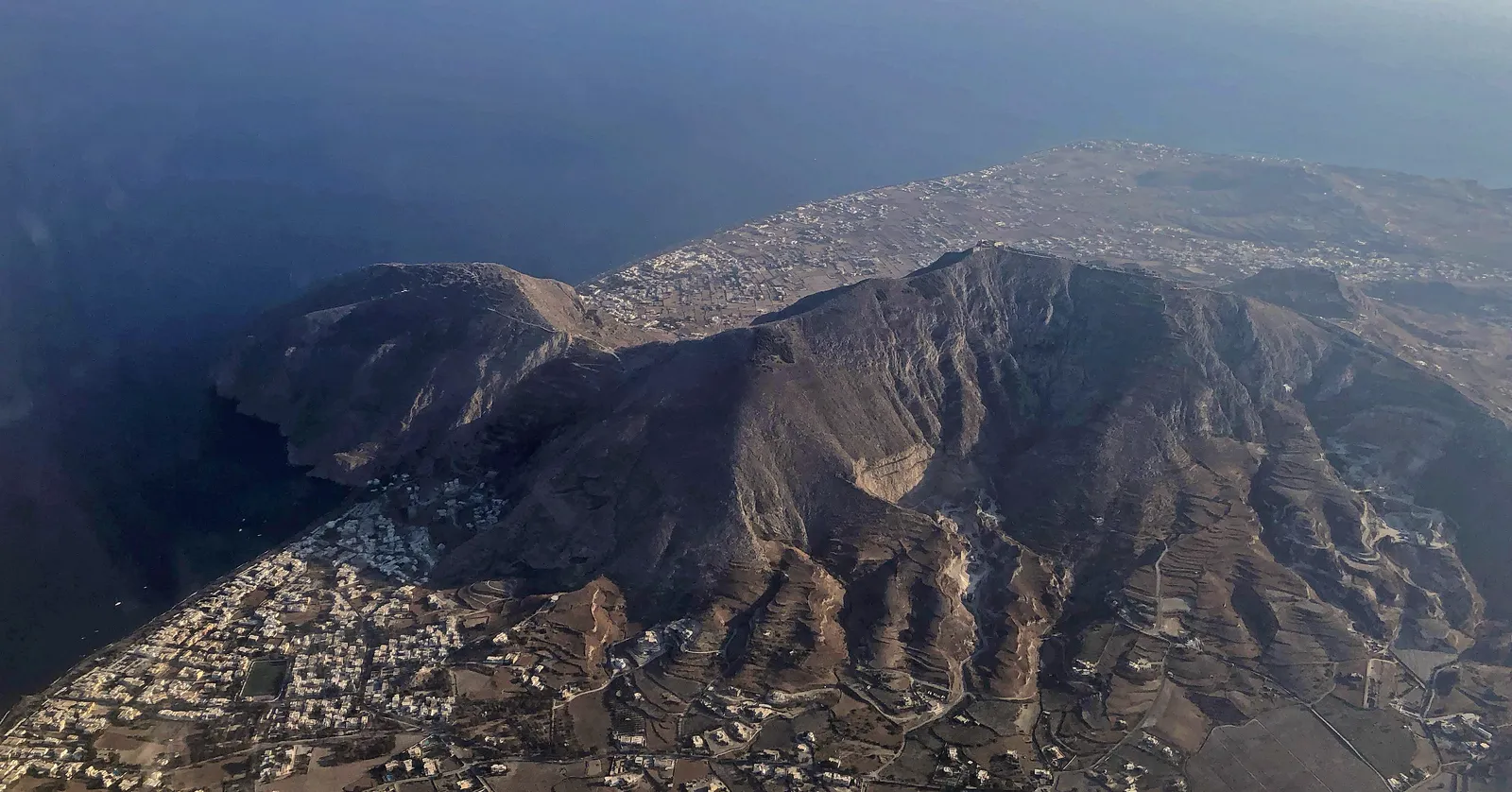 The dark headland of Mesa Vouno from the air, dropping into the sea with the built-up strip of Kamari along the coast on one side and Perissa on the other
