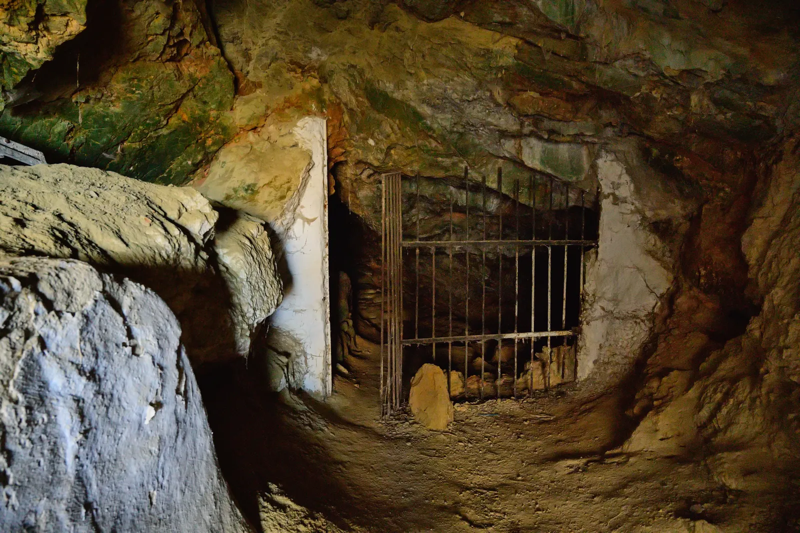 The barred entrance to the Zoodochos Pigi cave above Kamari, an iron gate set in whitewashed masonry inside a low opening in the limestone rock face