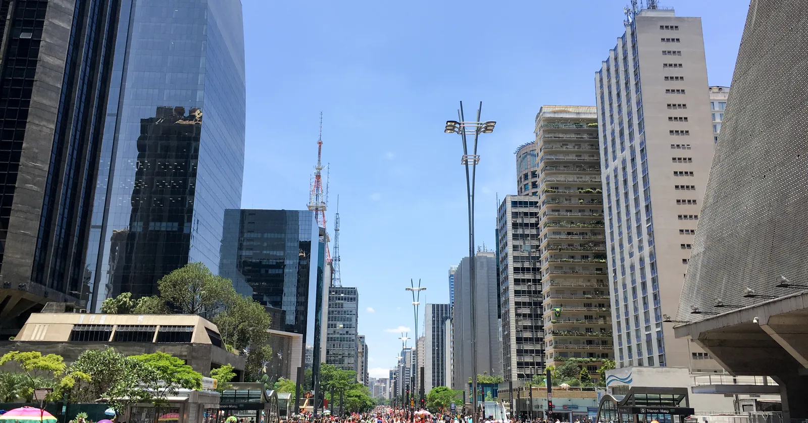 Avenida Paulista in São Paulo closed to traffic, with people walking and cycling down the middle of the roadway between office towers, trees along the central reservation and a radio mast on the skyline