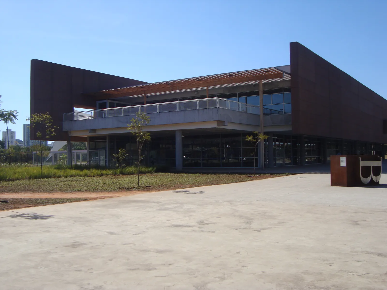 The Biblioteca de São Paulo in the Parque da Juventude, a low rust-coloured building with a projecting upper storey and a long balcony, standing on open ground under a clear sky