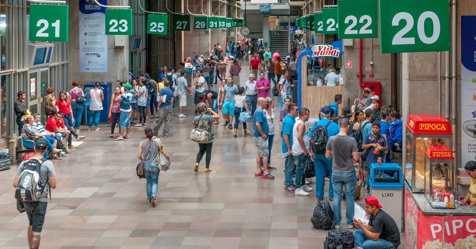 The concourse of the Tietê coach terminal in São Paulo, a long hall with numbered green gate signs hanging above the boarding doors on the right and crowds of travellers with bags moving down the middle