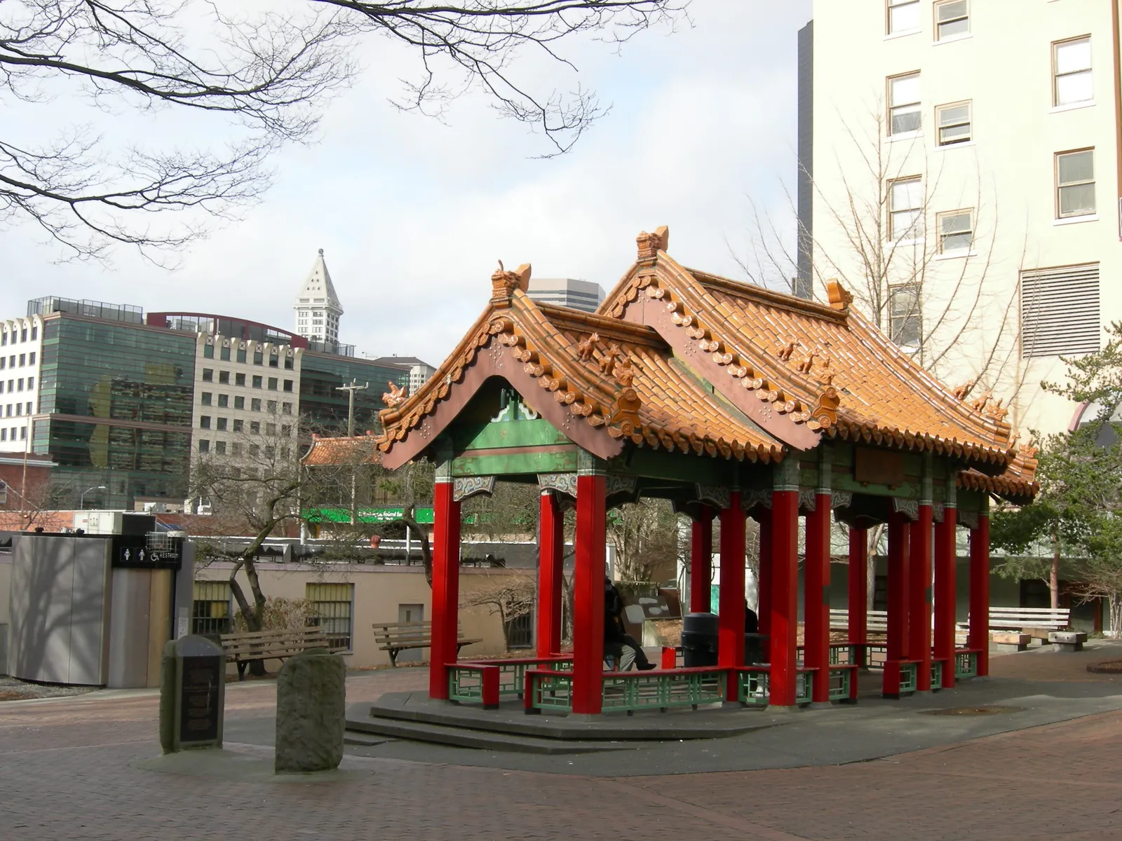 The Grand Pavilion in Hing Hay Park, Seattle, an open shelter on red columns with tiled upswept roofs, with Smith Tower visible behind it