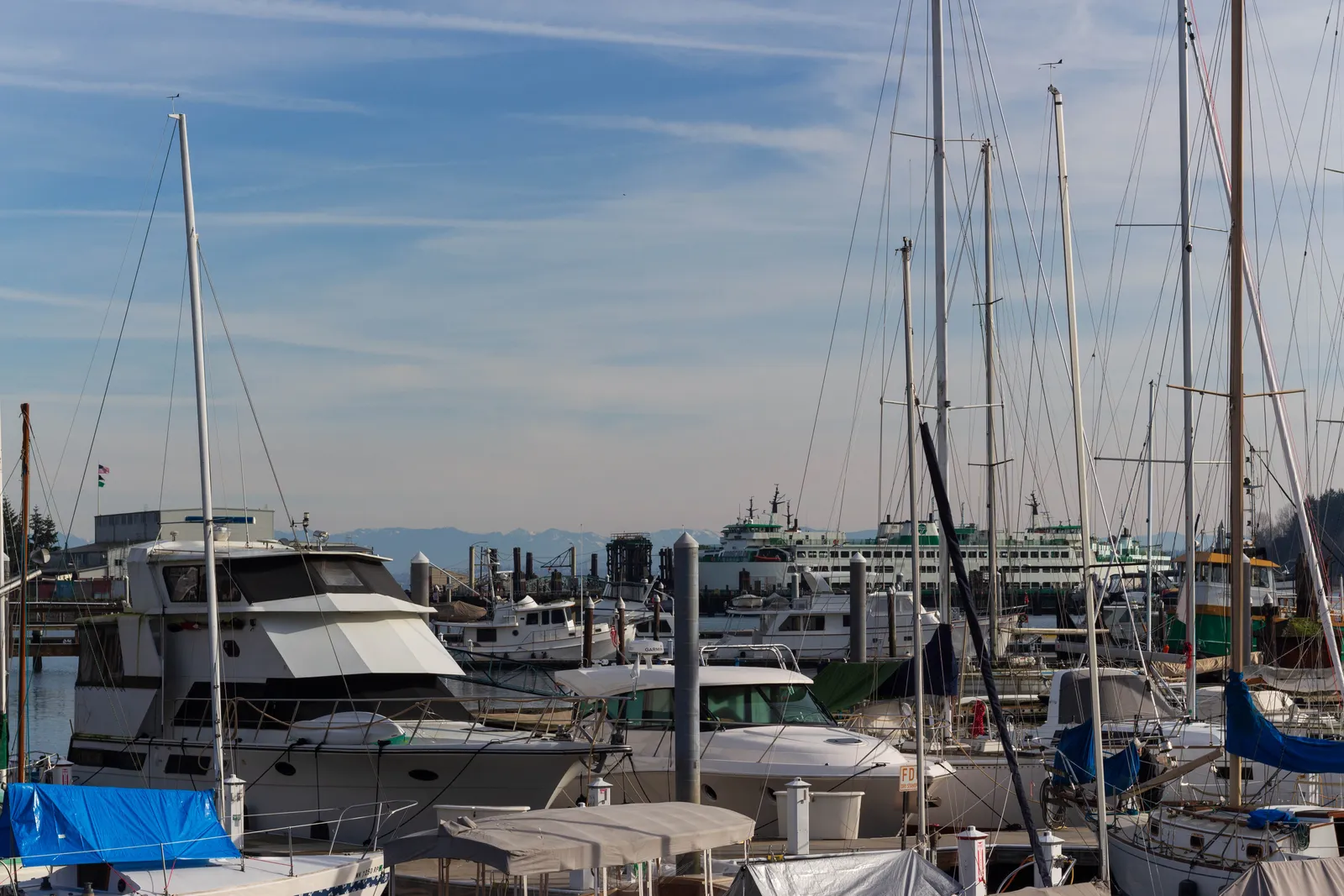 Sailing boats and cruisers moored in Eagle Harbor at Winslow on Bainbridge Island, with a green and white ferry crossing behind the masts