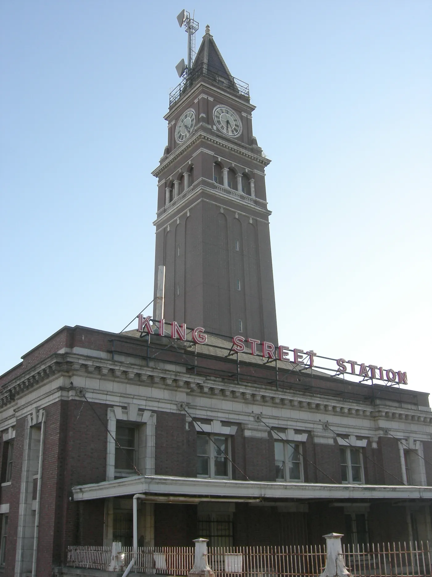 King Street Station's brick clock tower in Seattle rising above the station's red neon roof sign, with the four-faced clock near the top
