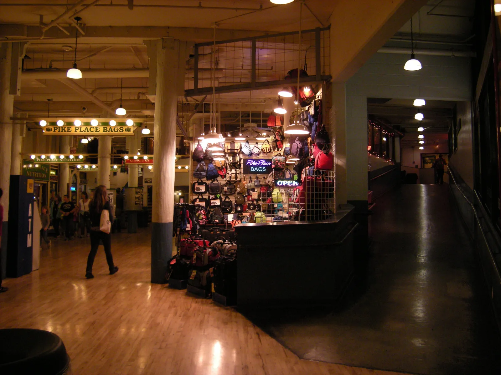 A lit corridor of small shops on one of the DownUnder levels beneath Pike Place Market's Main Arcade, with a Pike Place Bags sign at the far end
