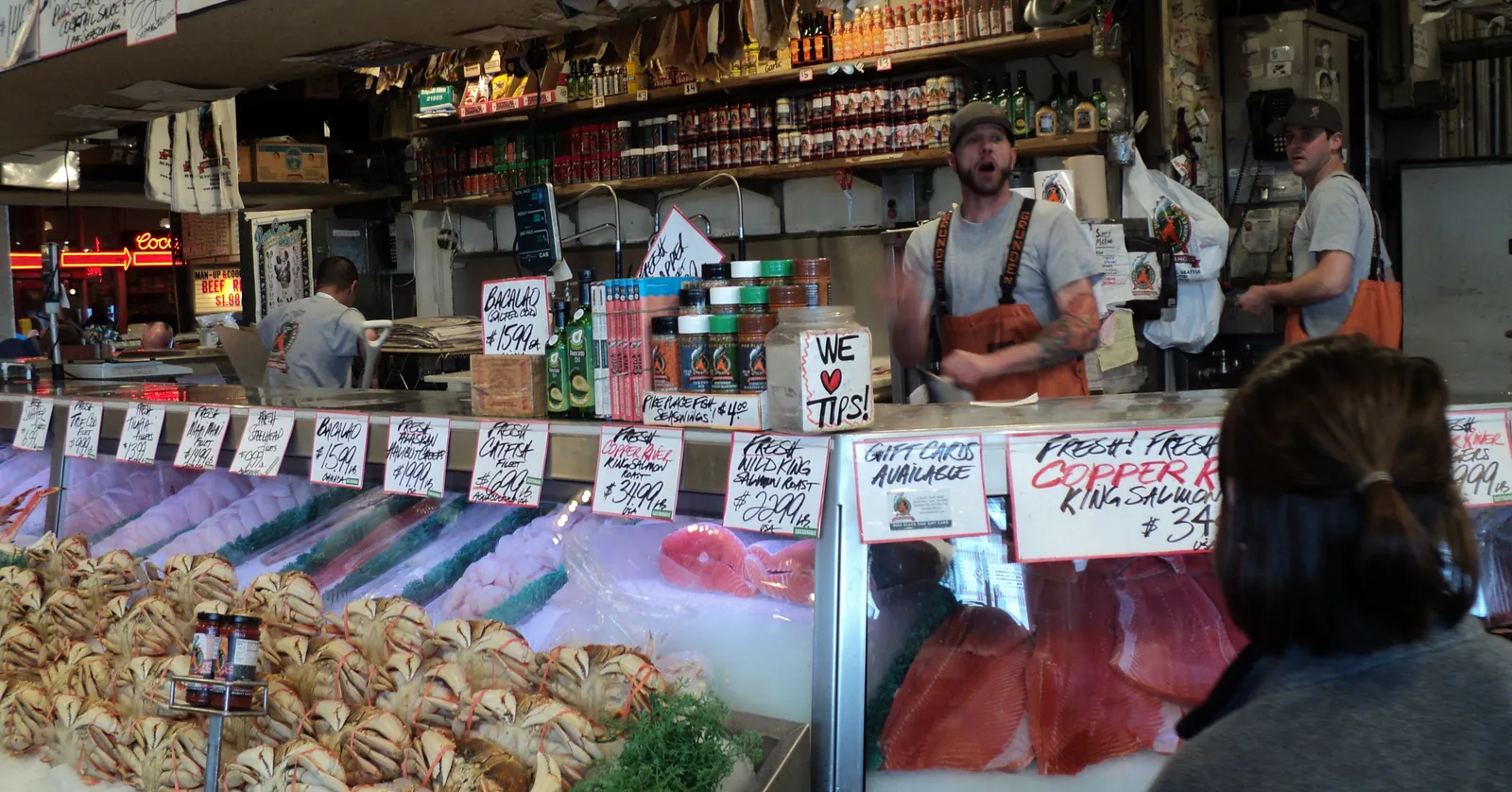 The Pike Place Fish Market counter in Seattle, with crab and whole salmon laid out on ice under hand-lettered price signs and fishmongers working behind it