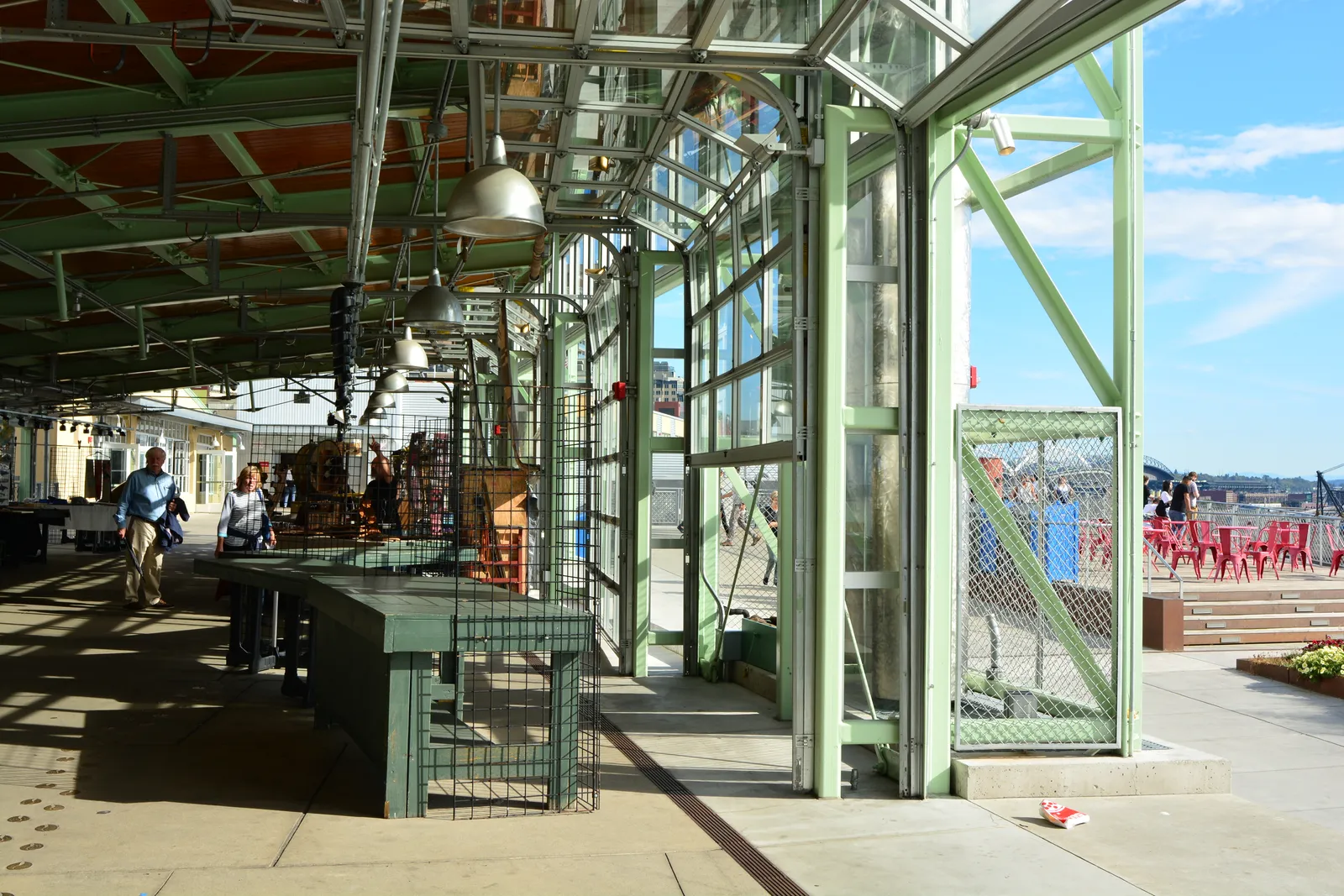 The covered MarketFront pavilion at the north end of Pike Place Market, its green steel frame open along one side to a terrace and Elliott Bay beyond
