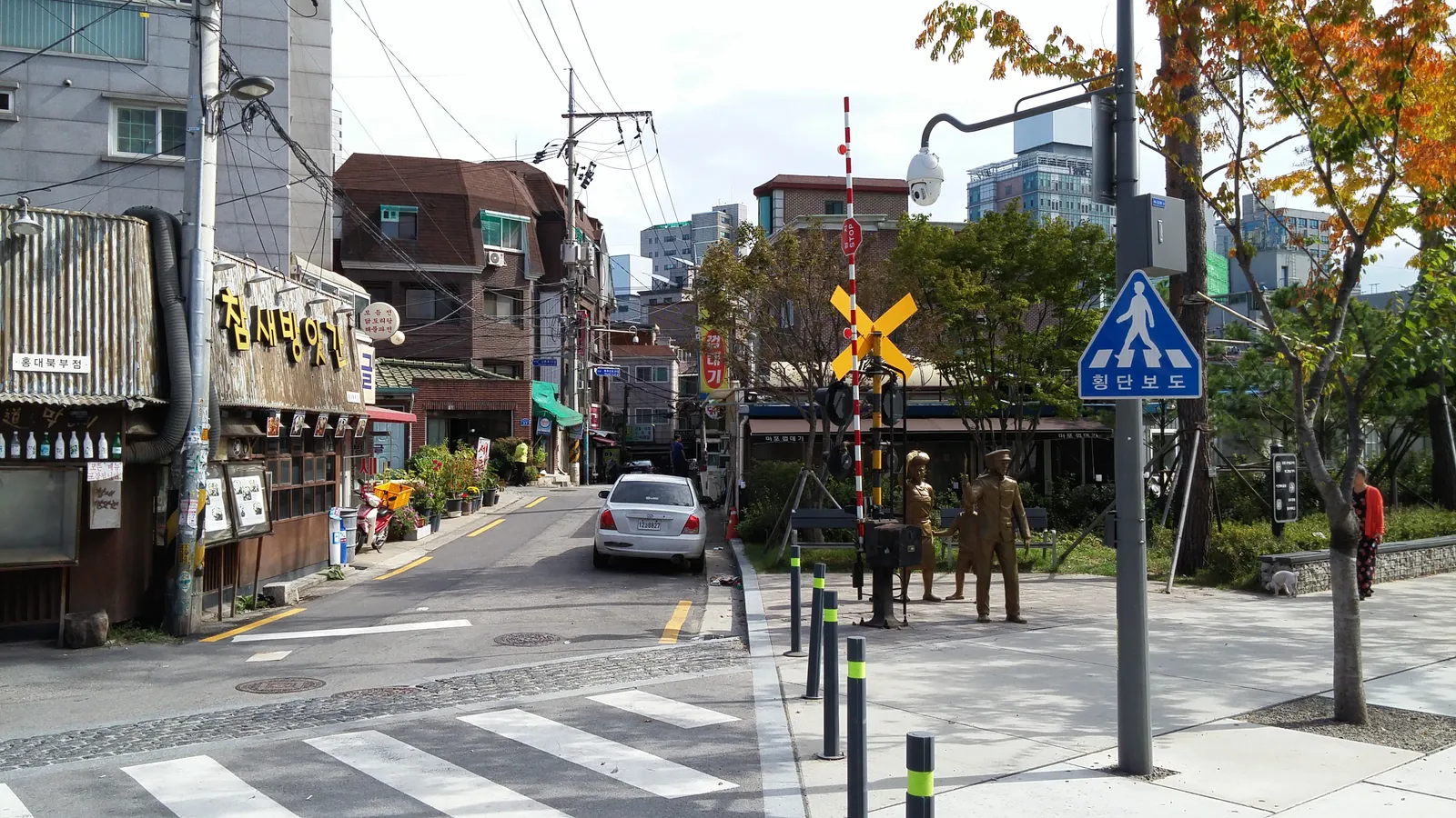 The old railway crossing at Ttaeng-ttaeng Street near Hongdae in Seoul, a crossbuck sign and a short length of track kept beside the road, with small bars and shops behind
