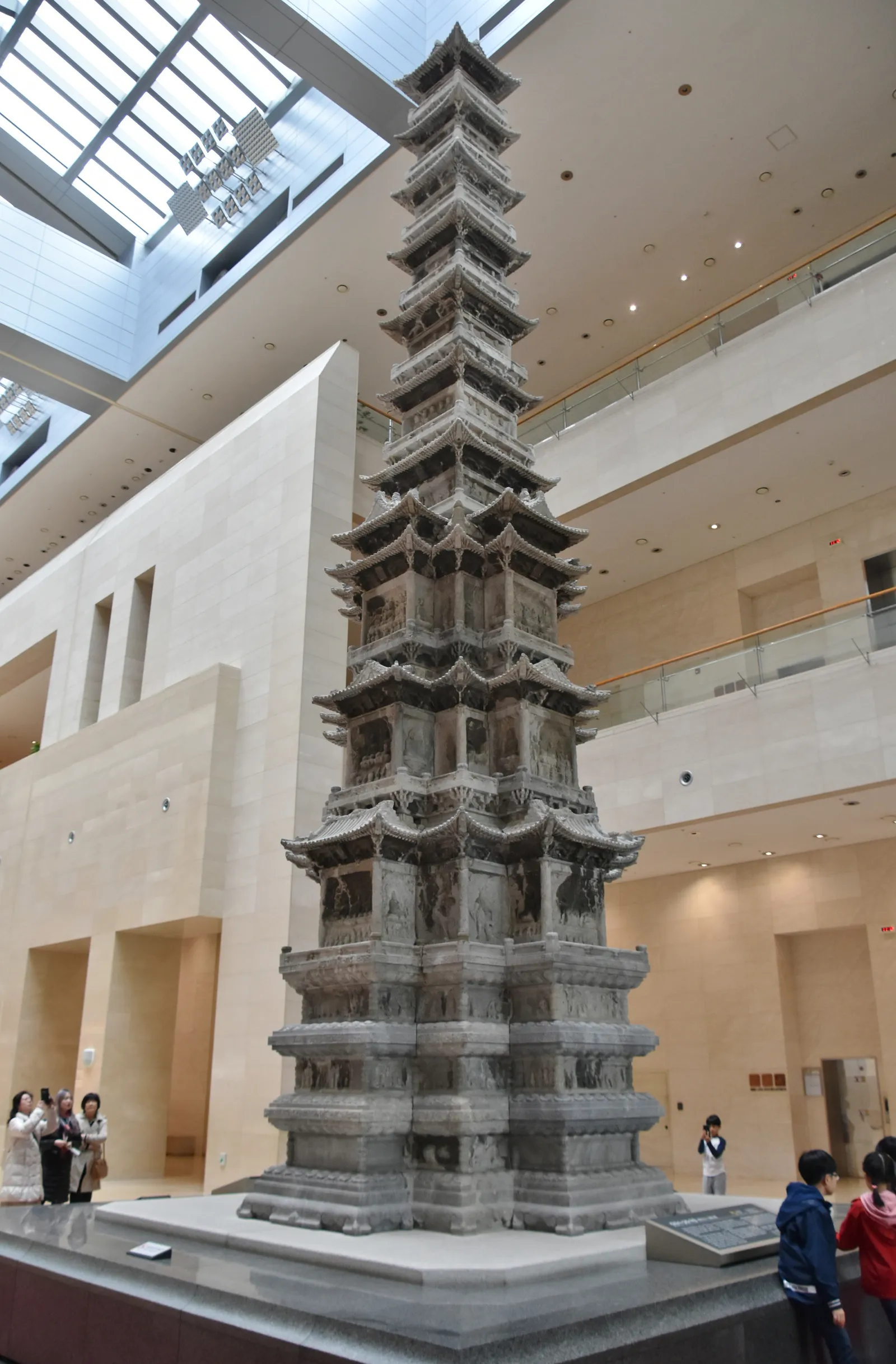 The ten-storey grey marble pagoda from Gyeongcheonsa temple standing in a tall skylit hall at the National Museum of Korea in Seoul, carved with figures on every level