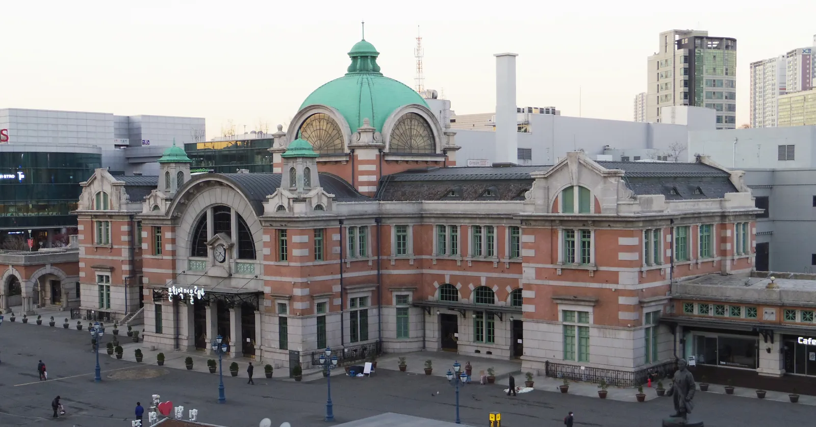 The old Seoul Station building of 1925, red brick banded with grey stone under a green copper dome, facing an open plaza in central Seoul