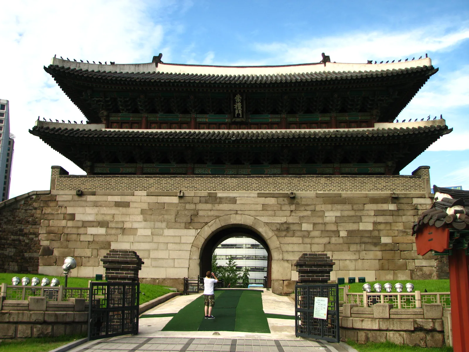Sungnyemun, Seoul's old south gate, a two-storey wooden pavilion with tiled roofs on a massive stone base pierced by an arched passage, behind an iron fence and a lawn