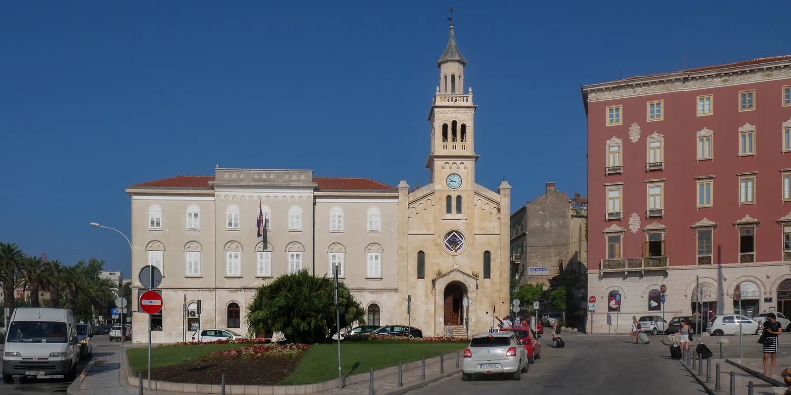 The church and monastery of St Francis in Split seen from the street, a pale stone church front with a rose window and a slim open bell tower, the monastery building beside it and a red palazzo on the corner