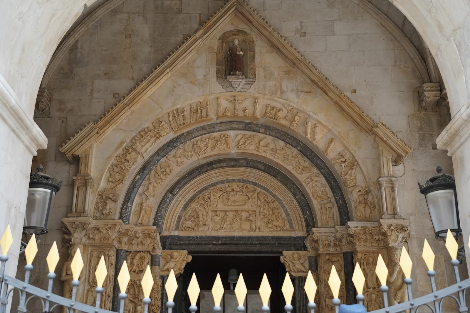 The carved stone doorway of Trogir cathedral, a deep Romanesque arch of concentric carved bands crowded with small figures and animals, set under a pointed gable in a pale stone wall