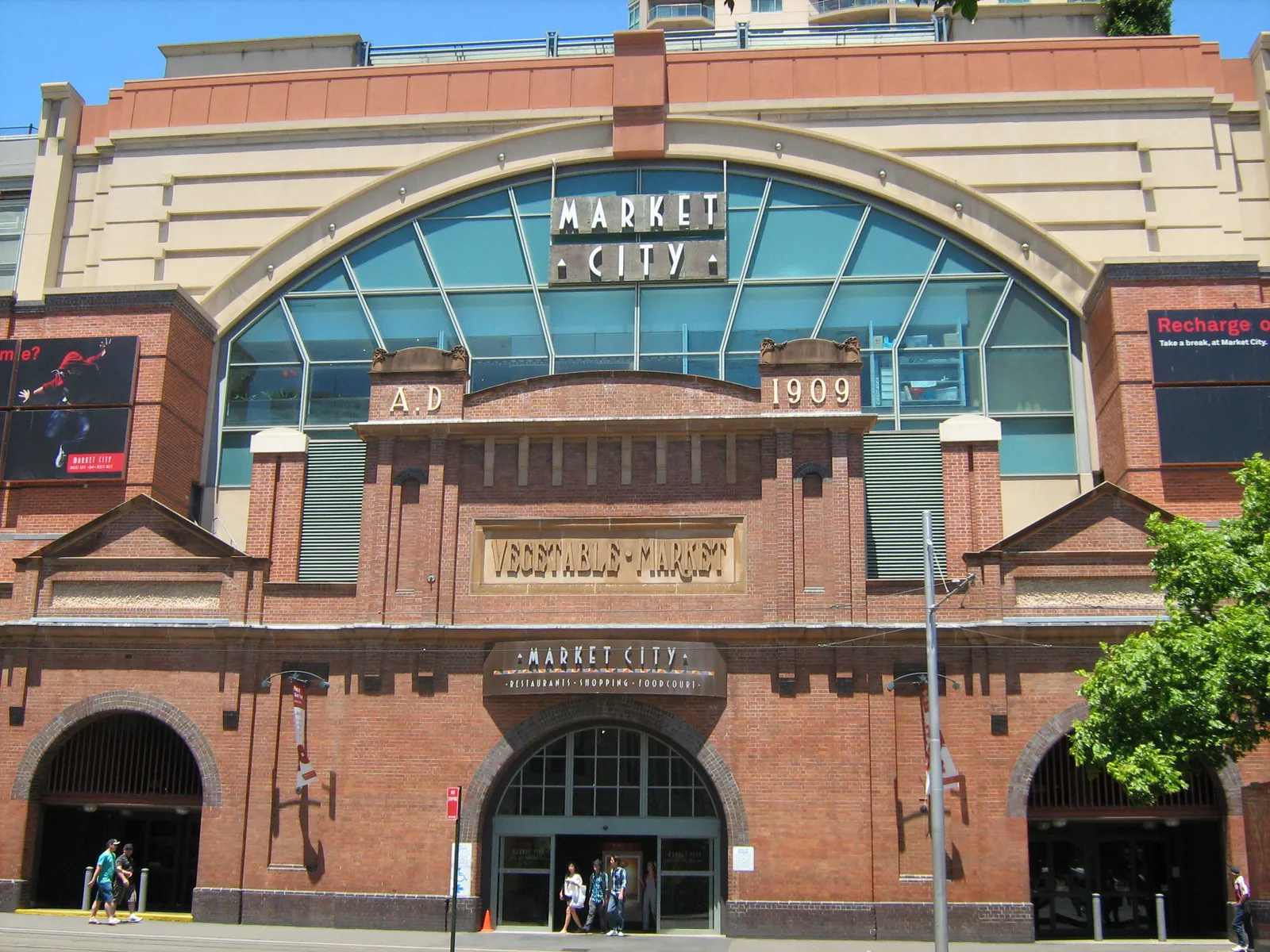 The red-brick Hay Street entrance of Market City in Haymarket, Sydney, with its arched glass window and a 1909 date stone over the doors to Paddy's Markets