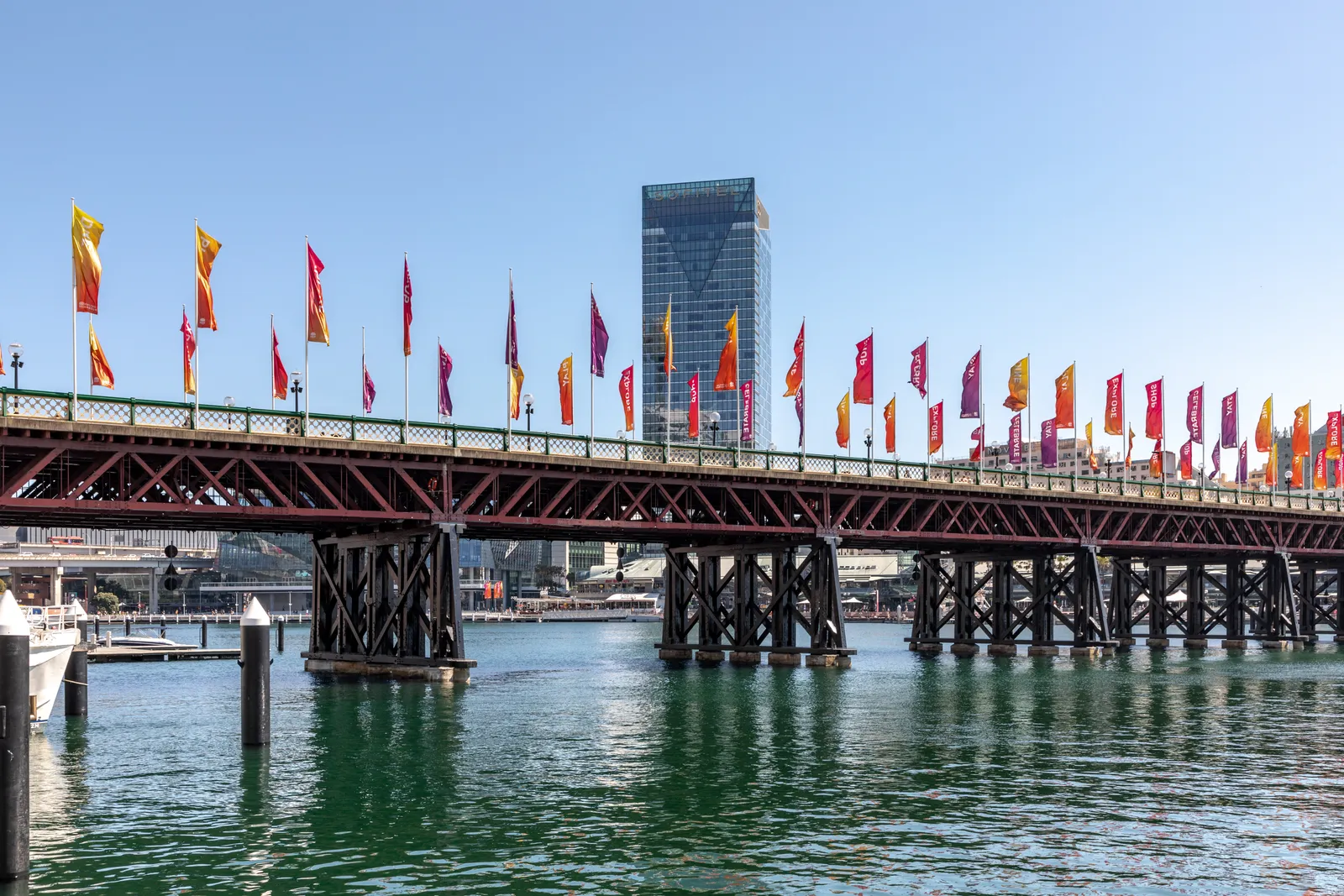 Pyrmont Bridge crossing Darling Harbour in Sydney on its timber piers, a row of coloured flags along its railing and a city tower behind