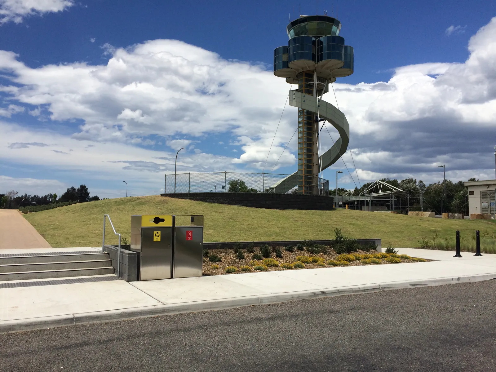 The grassed lookout mound at Shep's Mound beside Sydney Airport, with the airport's air traffic control tower and its spiral stair rising behind it