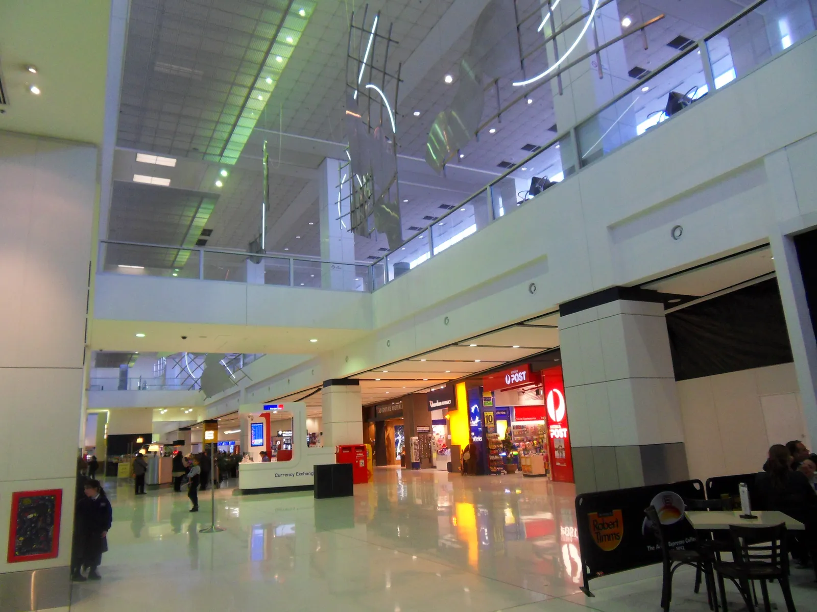 The landside hall of Sydney Airport's international terminal, a tall atrium with a mezzanine walkway above cafes and shopfronts on the ground floor