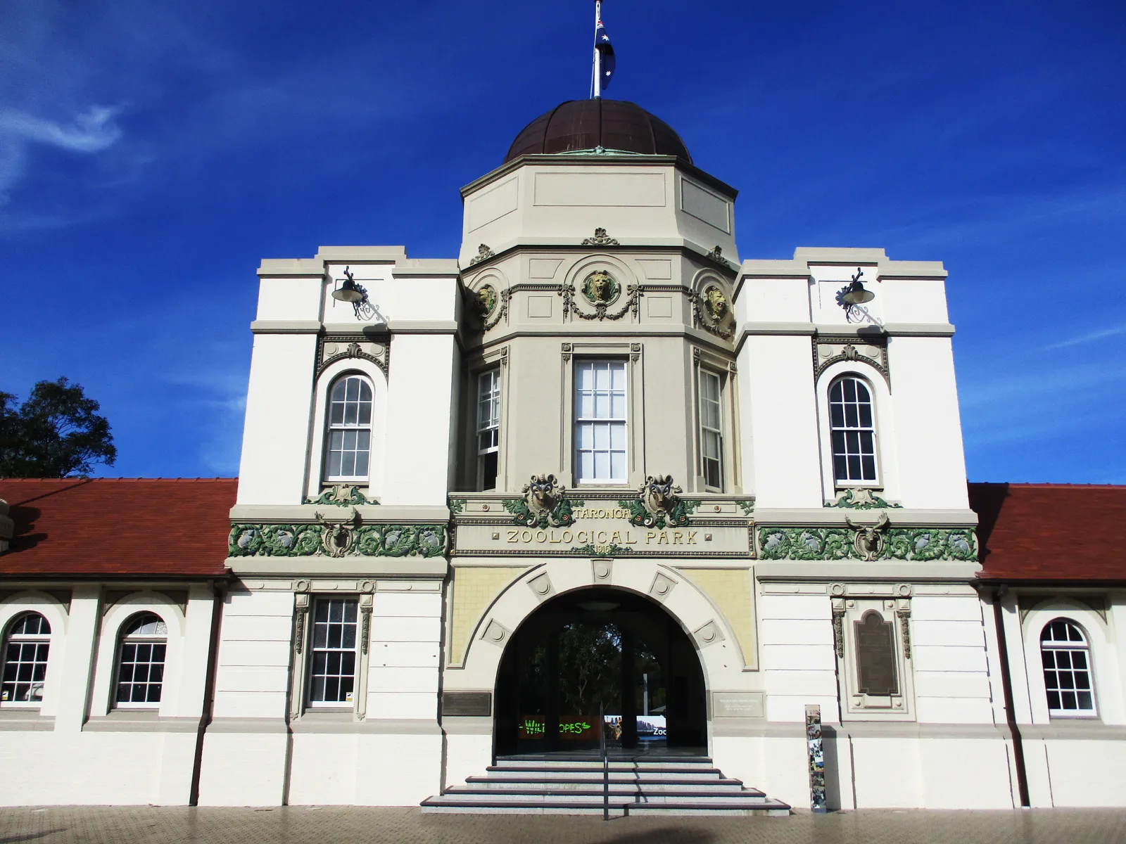 The cream-painted top entrance building of Taronga Zoo in Sydney, with a domed tower over an arched doorway and red-tiled wings either side