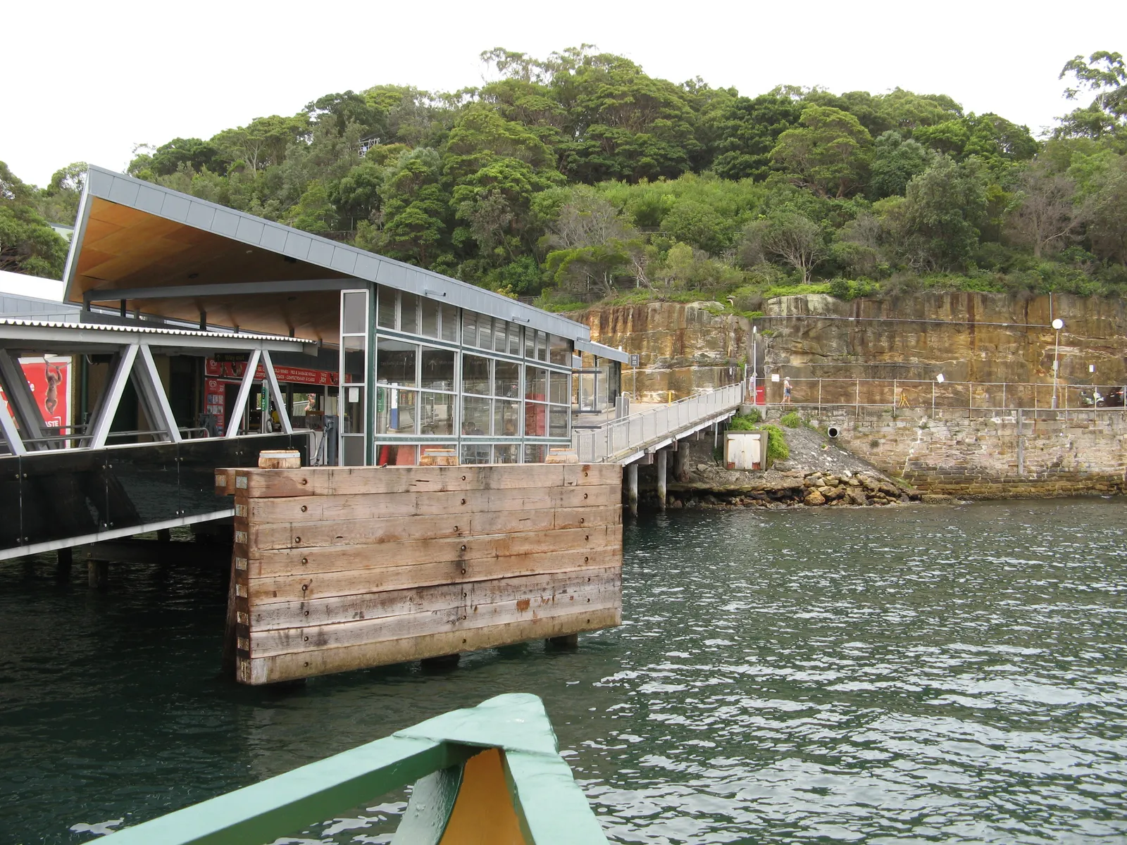 Taronga Zoo ferry wharf in Mosman seen from an arriving ferry, a covered pontoon at the foot of a wooded sandstone slope