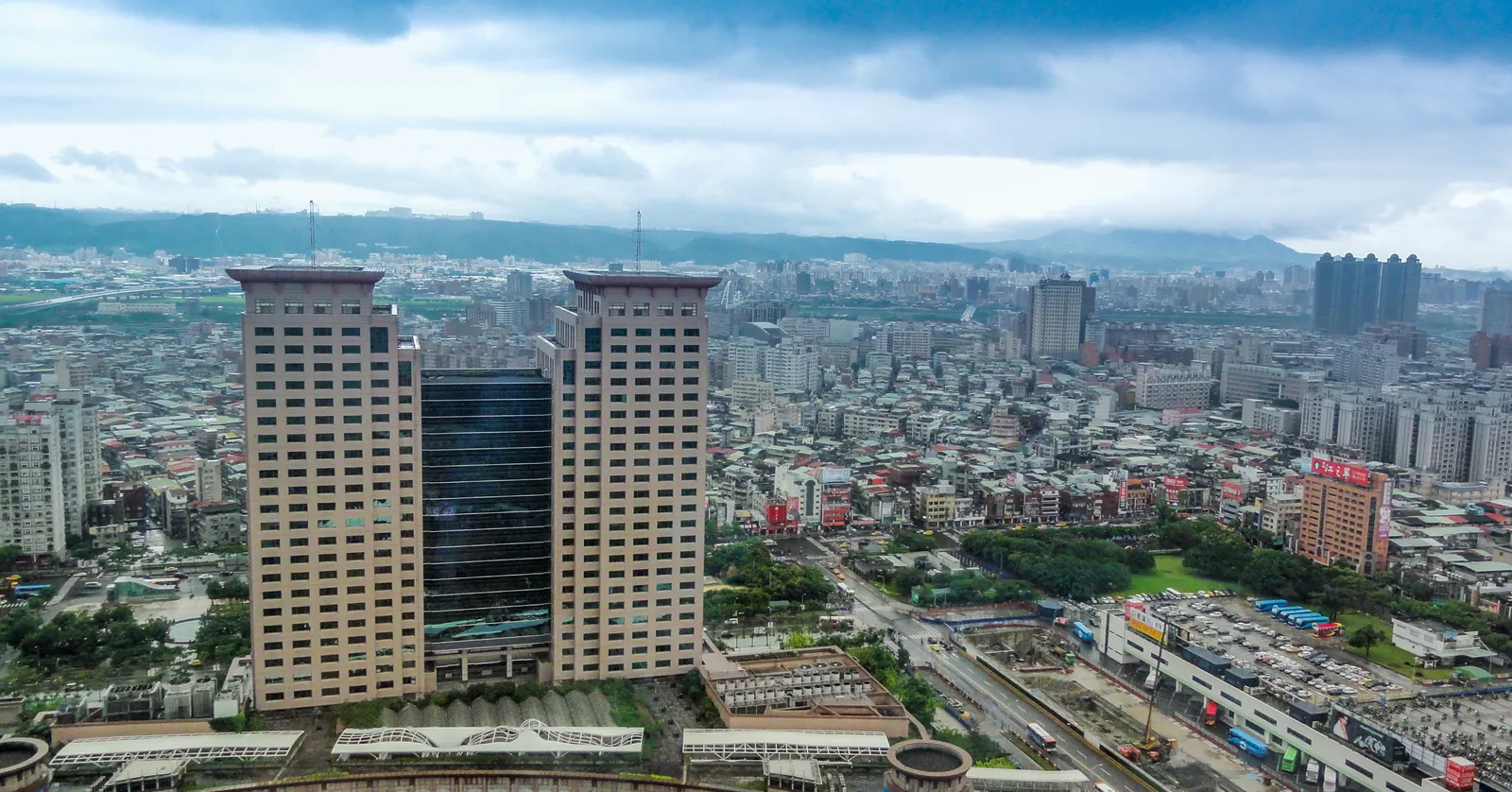 The twin towers of the Banqiao Station complex in New Taipei seen from the air, standing over the low rooftops of the surrounding district with hills on the horizon