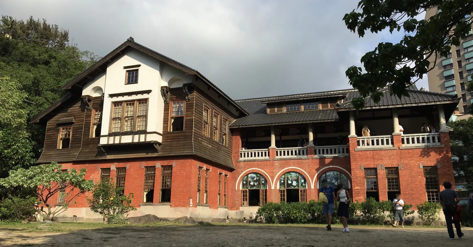 The Beitou Hot Spring Museum in Taipei, a 1913 bathhouse with an arcaded red brick ground floor and a white and dark timber upper storey, set among trees