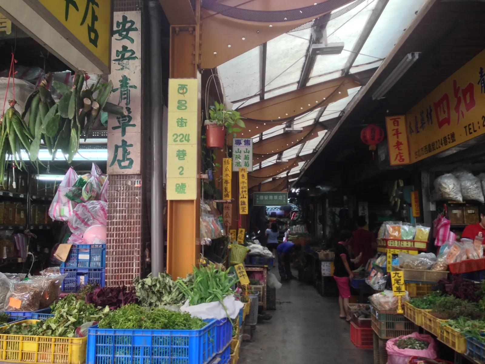Herb Alley beside Longshan Temple in Taipei, a covered lane with crates of fresh green herbs stacked outside shops and a street sign reading Lane 224, Xichang Street