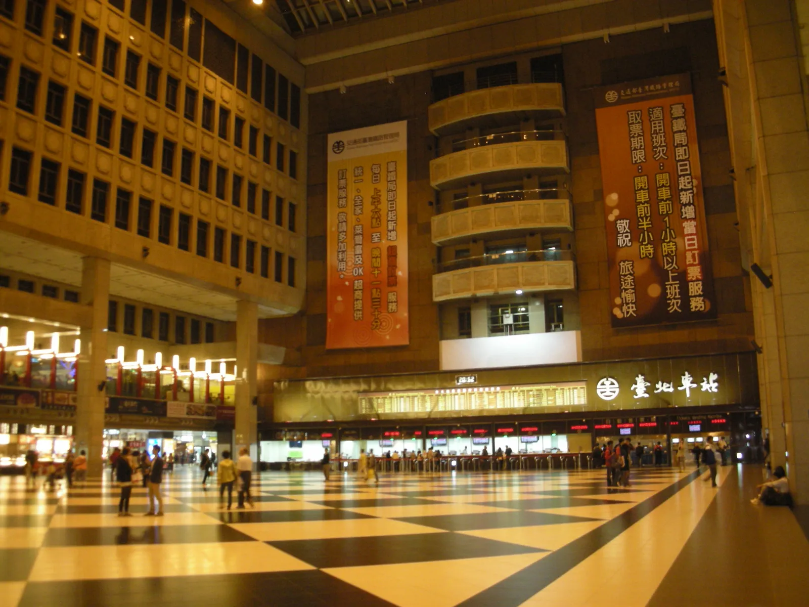 The great hall of Taipei Main Station, a tall atrium with a black-and-white chequerboard floor, ticket windows along the far wall and the station's name sign above them