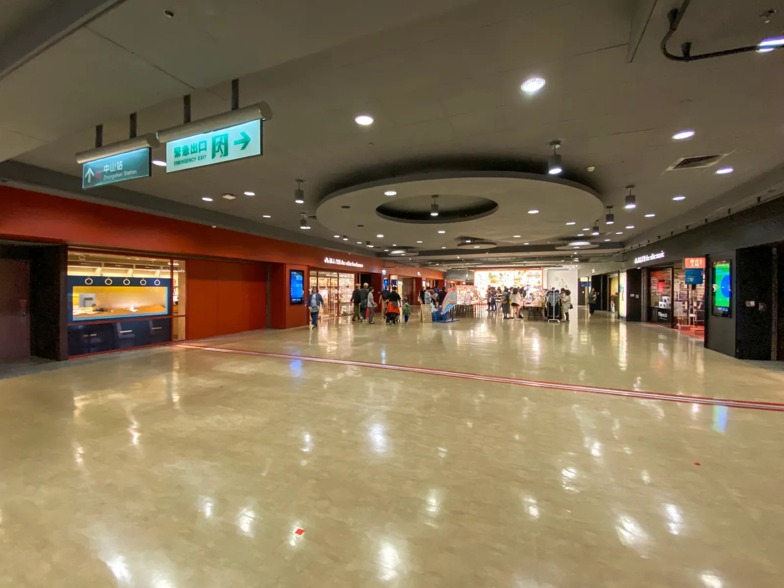 A wide underground shopping corridor in Taipei's Zhongshan Metro Mall, shopfronts down both sides under a low lit ceiling and a polished floor running into the distance