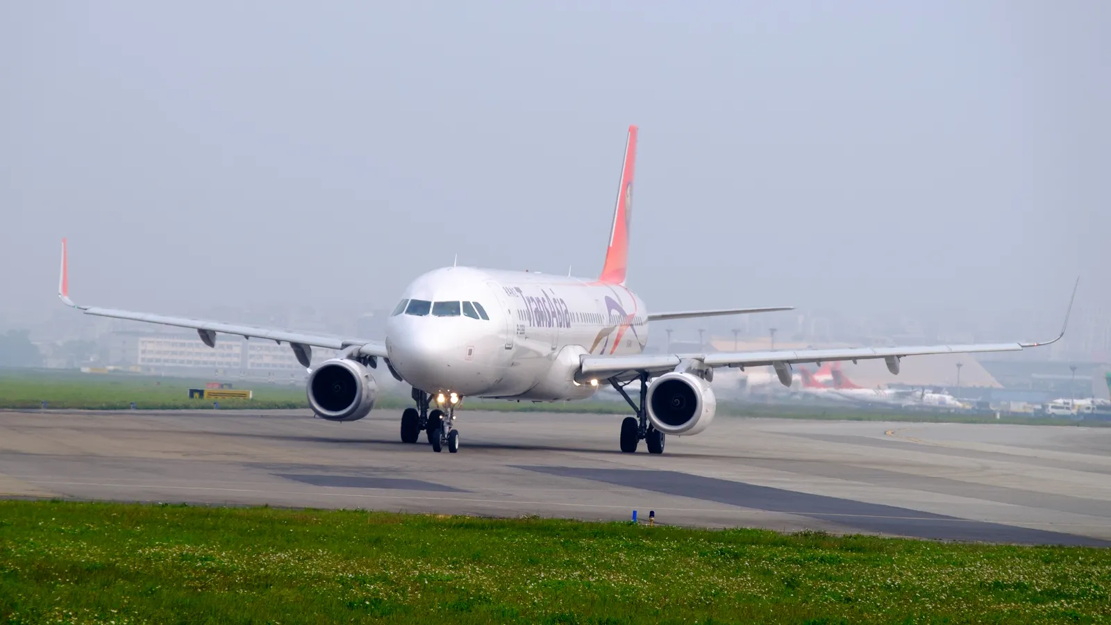 An airliner turning onto the runway at Taipei Songshan Airport, seen low across a grass verge with the airfield stretching away behind it