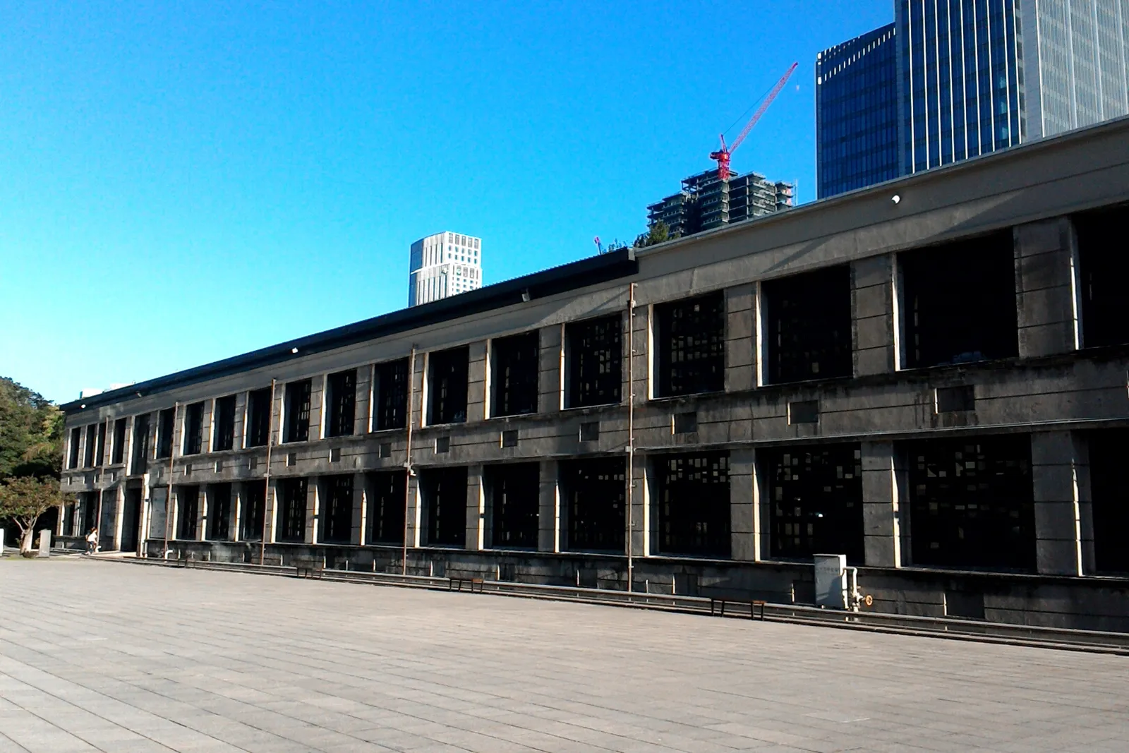 The long north facade of the former Songshan tobacco factory in Taipei, a two-storey concrete building with rows of tall windows above an empty paved forecourt