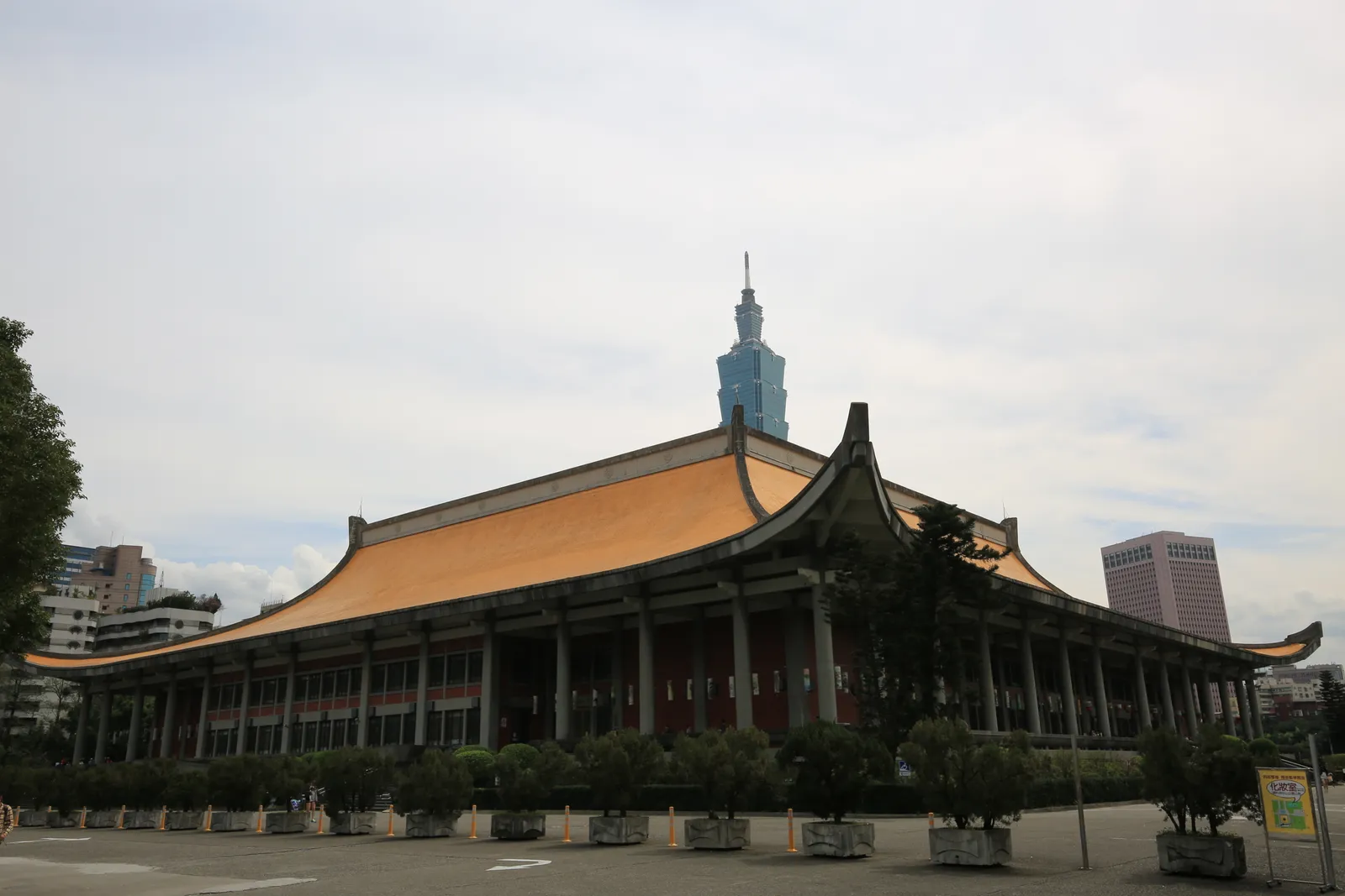 The Sun Yat-sen Memorial Hall in Taipei, a broad hall under a sweeping yellow tiled roof on square columns, with Taipei 101 rising directly behind it
