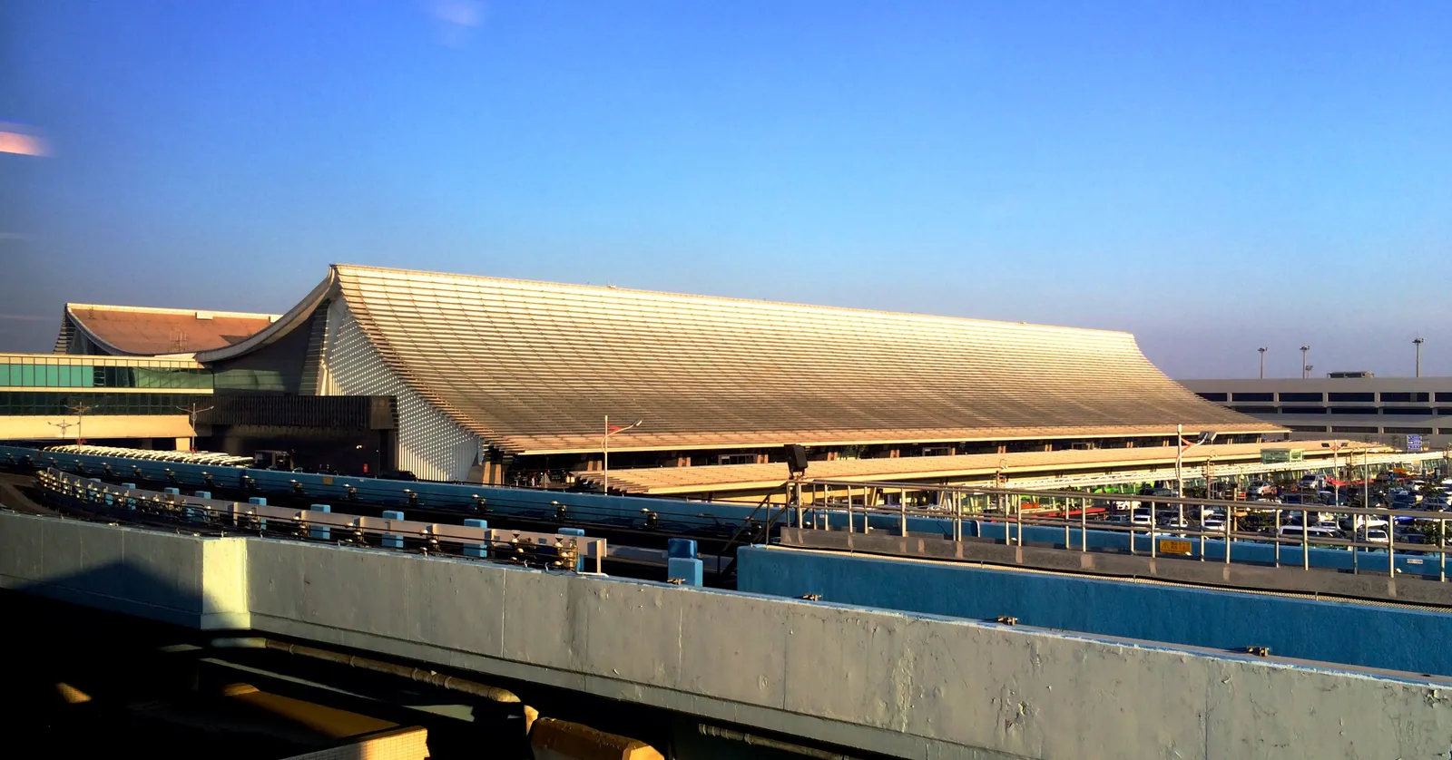 The curved golden roof of Terminal 1 at Taiwan Taoyuan International Airport in late afternoon light, with the elevated departures road running in front of it
