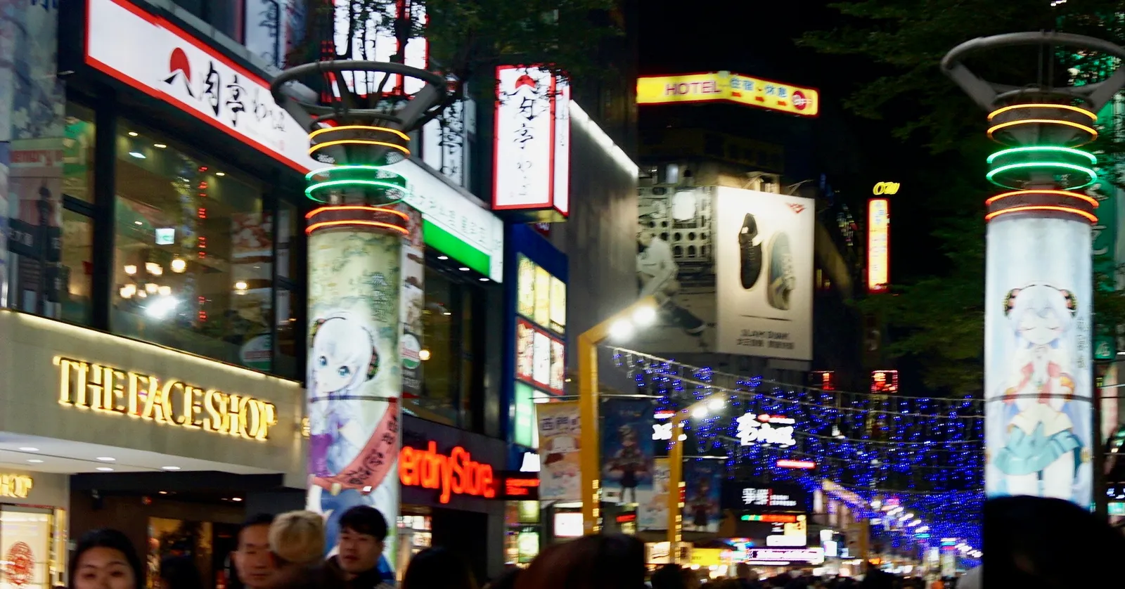 A street in Ximending, Taipei, at night, lined with lit shopfronts, illuminated advertising columns and vertical neon signs, with a crowd walking down the middle