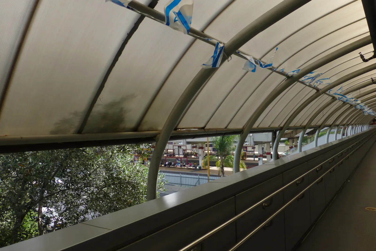 The glazed barrel-vaulted footbridge at Tel Aviv Savidor Center station, its steel ribs curving overhead and the motorway and city visible through the glass along one side